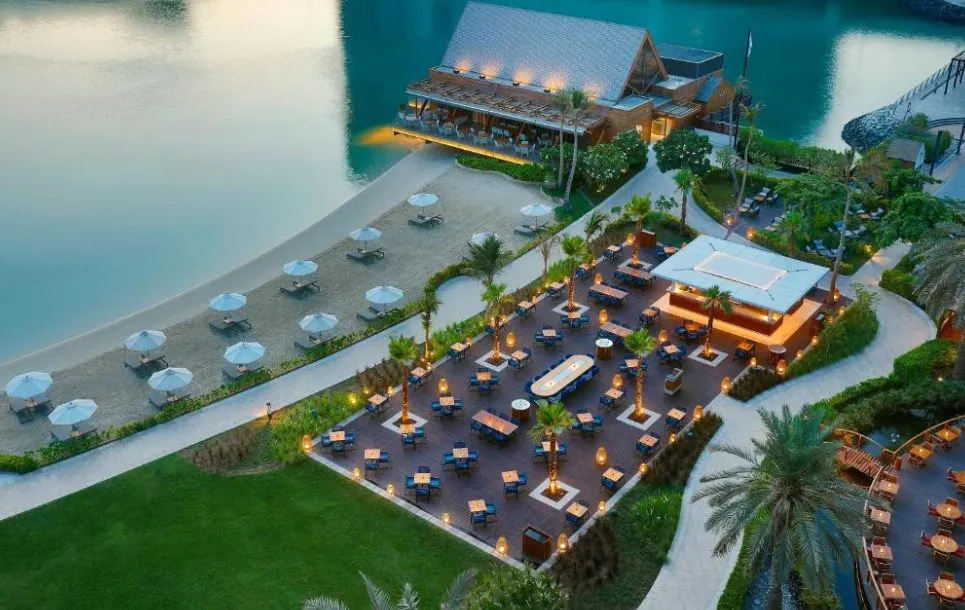 Beach Rotana Abu Dhabi mit privatem Strandbereich und Outdoor-Restaurant am Wasser bei Abendlicht