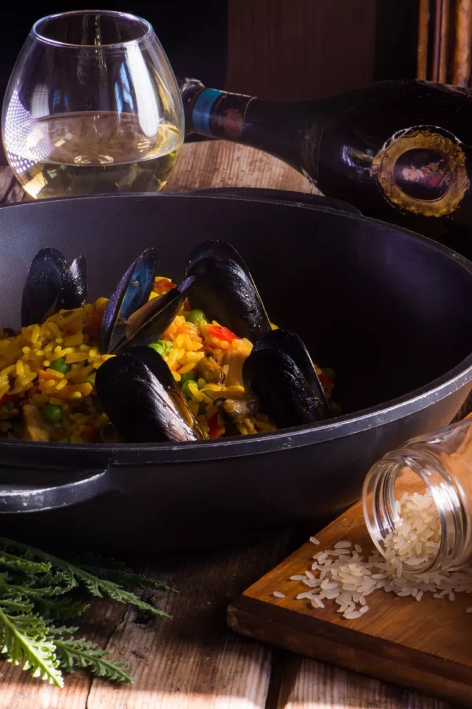 Muscheln essen – Paella mit Miesmuscheln im gusseisernen Topf, daneben Weißwein und Reis