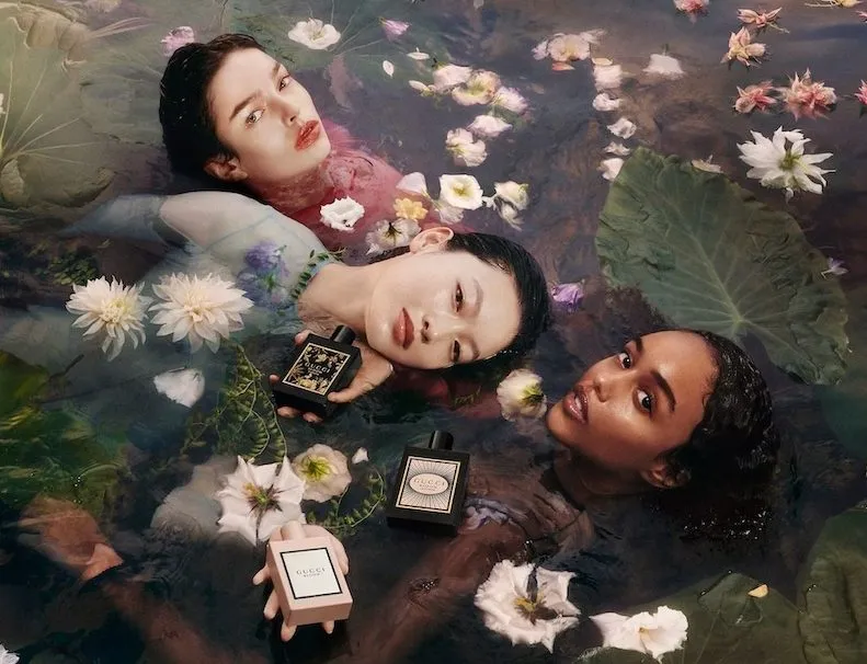 Gucci Parfums – drei Models liegen zwischen Wasserblüten im Wasser und halten Flakons; poetische, florale Kampagnenästhetik.