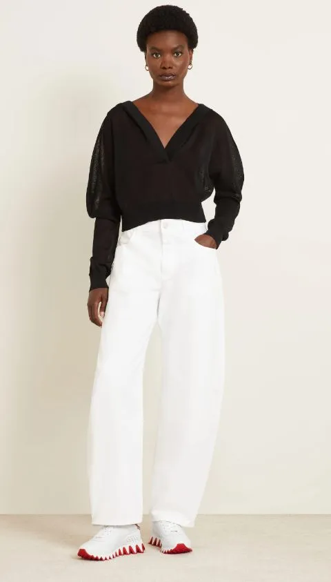 Frau in weitem weißen Denim und schwarzem Pullover, kombiniert mit weißen Louboutin-Sneakers mit roter Sohle – moderner, lässiger Look.