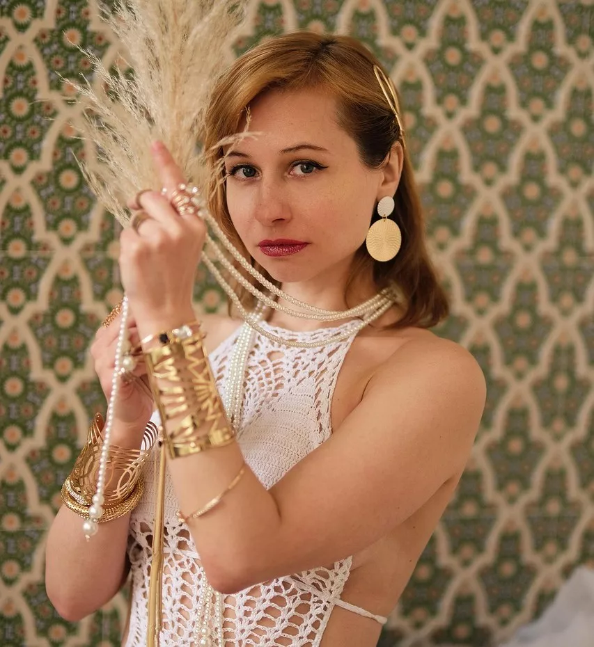 Stilvolle Frau im Boho-Luxus-Look mit weißen Häkel-Details, goldenen Schmuckstücken, auffälligen Ohrringen und glamourösem Lippenstift.