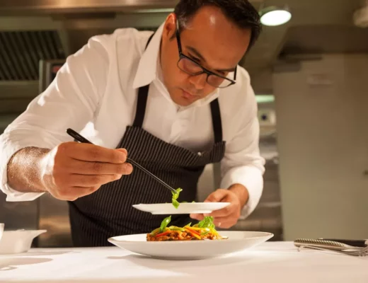 Koch in weißer Uniform richtet ein Gourmetgericht präzise mit Pinzette an – Fine Dining im Restaurant mit Michelin Stern Ulm.