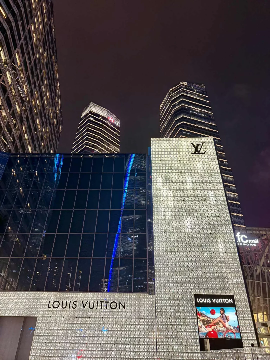 China Reise -Beleuchteter Louis Vuitton Store in Shanghai bei Nacht mit modernen Hochhäusern im Hintergrund