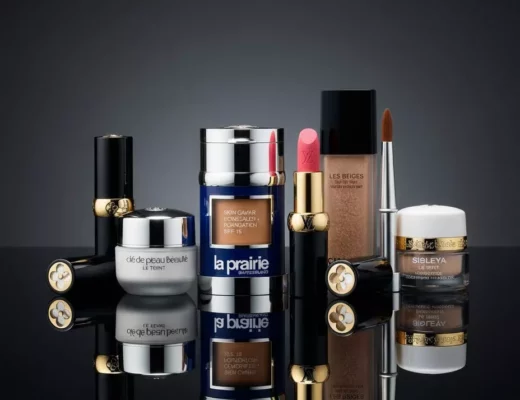 Teuerste Make-up-Marke der Welt – Ensemble aus La Prairie Skin Caviar Concealer–Foundation, Louis-Vuitton-Lippenstift, Chanel Les Beiges Eau de Teint mit Pinsel, Clé de Peau Beauté und Sisleÿa Le Teint auf spiegelnder, schwarzer Fläche.