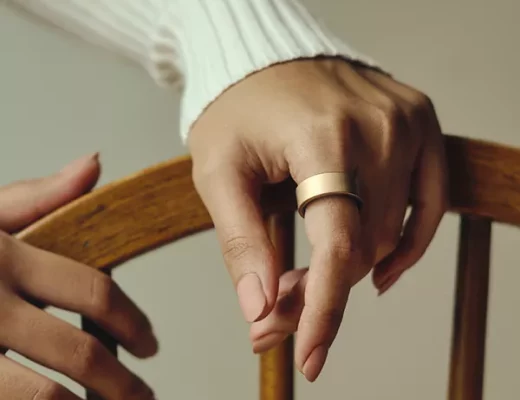 Hand mit goldenem Ultrahuman Ring AIR, getragen als luxuriöses Schmuckstück auf einem Holzstuhl