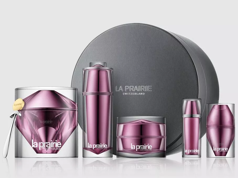 Dieses Stillleben stellt die Suche nach der teuersten Make-up-Marke der Welt visuell dar: Im Zentrum steht La Prairie mit der Skin Caviar Concealer–Foundation, flankiert von einem Louis-Vuitton-Lippenstift im Schwarz–Gold-Design, Chanel Les Beiges Eau de Teint samt Pinsel, einem Clé de Peau Beauté Tiegel und Sisleÿa Le Teint. Die spiegelnde, schwarze Fläche betont Glas, Metall und Lack, während der dunkle Verlaufshintergrund den Luxuscharakter verstärkt. Das kuratierte Set eignet sich als Keyvisual für Rankings, Vergleiche und Artikel rund um High-End-Make-up.