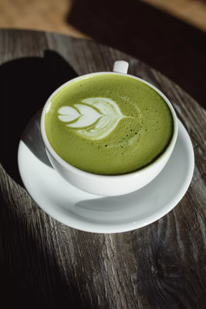 Heißer Matcha Latte in weißer Tasse mit Tulpen-Latte-Art auf rustikalem Holztisch.