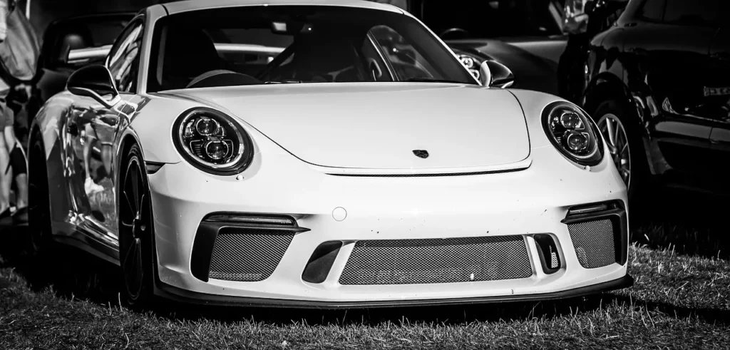 Schwarz-weiß Fotografie eines weißen Porsche 911 GT2 RS aus der Frontansicht, geparkt auf einer Wiese.