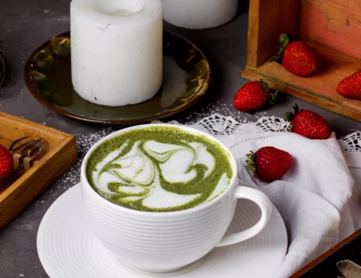 Heißer Matcha Latte mit marmorierter Latte-Art in weißer Rillentasse; Erdbeeren und Kerzen als Food-Styling.