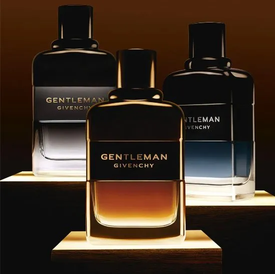 Drei Givenchy Gentleman Parfumflakons 2025 – amberfarbene, graue und blau-schwarze Duftvariante auf beleuchteten Podesten