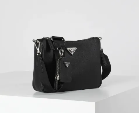 Schwarze Prada Herren-Umhängetasche aus Saffiano-Leder mit breitem Schulterriemen und abnehmbarem Mini-Pouch auf weißem Podest.