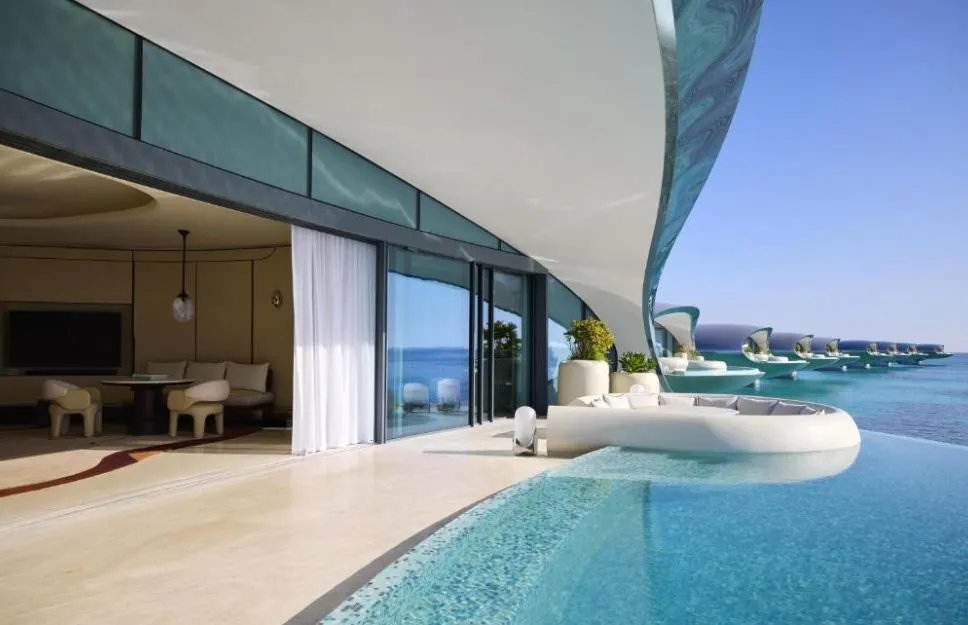 Terrasse einer Überwasser-Villa im Shebara Resort mit privatem Infinity-Pool, organisch geschwungener Dachkante und Blick auf die Reihe benachbarter Villen über dem Roten Meer.