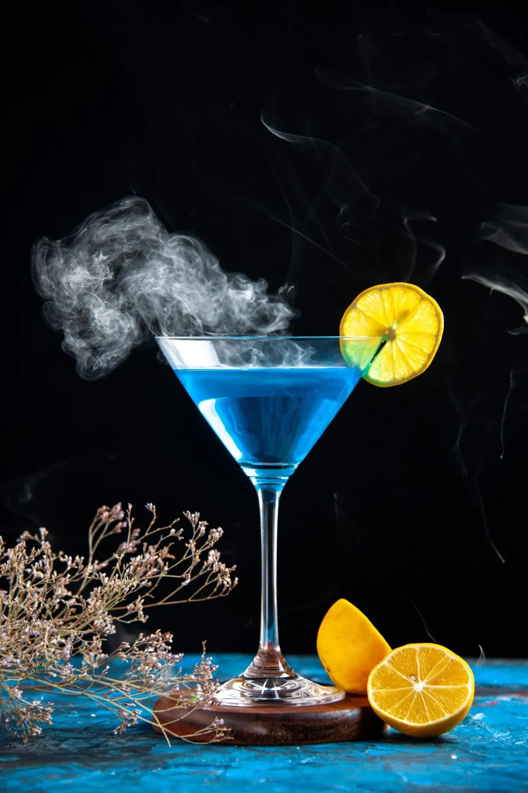 Blau leuchtender Gin-Cocktail im Martiniglas mit Zitronenscheibe und zartem Rauch vor schwarzem Hintergrund – Motiv zu der teuerste Gin der Welt