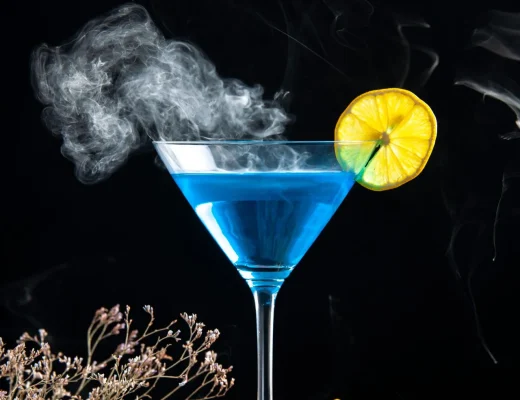 Blau leuchtender Gin-Cocktail im Martiniglas mit Zitronenscheibe und zartem Rauch vor schwarzem Hintergrund – Motiv zu der teuerste Gin der Welt