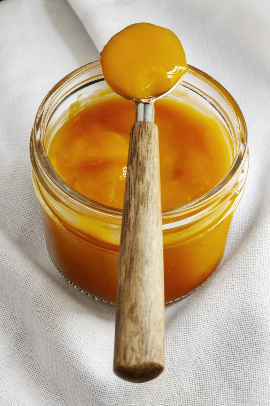 Cremiger Manuka Honig in einem offenen Glas, ein Holzlöffel liegt obenauf mit einer Portion Honig