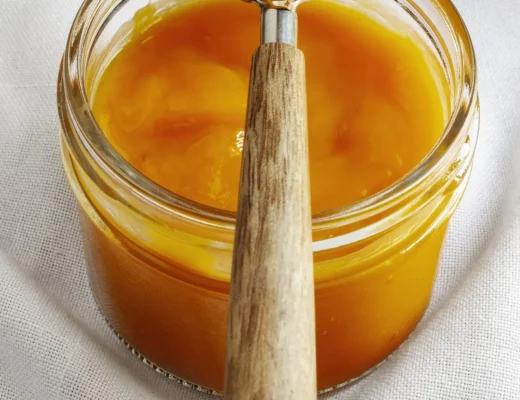 Cremiger Manuka Honig in einem offenen Glas, ein Holzlöffel liegt obenauf mit einer Portion Honig