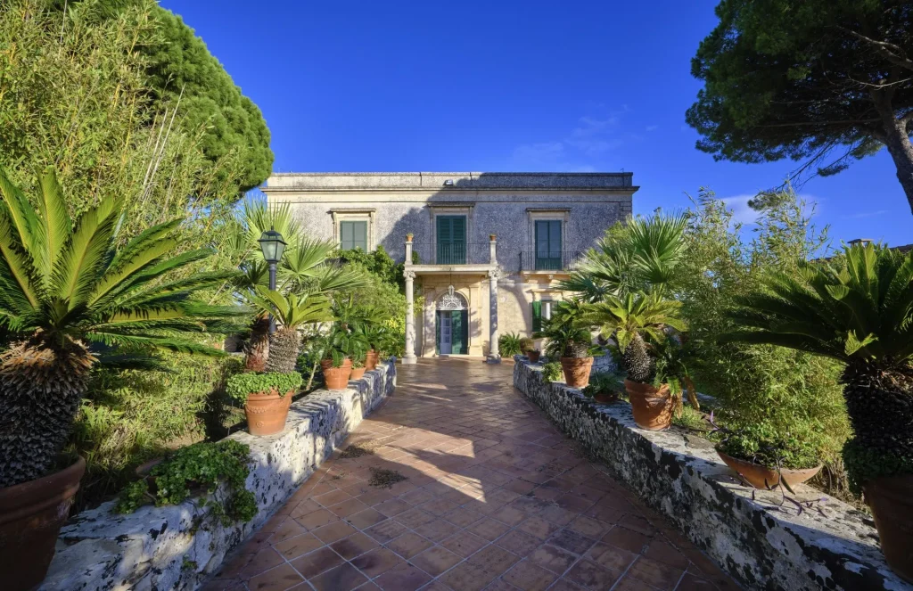 Exklusive Immobilien in Italien – historisches Herrenhaus aus Naturstein mit Palmenallee, Terrakottabelag und klassischer Fassade in Sizilien.