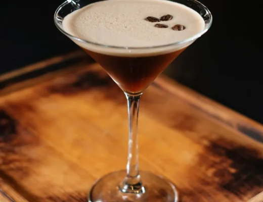 Espresso Martini im eleganten Martiniglas mit dichter Crema und drei Kaffeebohnen, serviert auf einer dunklen Holzplatte.