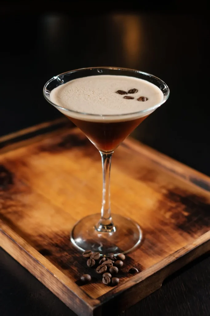 Espresso Martini im eleganten Martiniglas mit dichter Crema und drei Kaffeebohnen, serviert auf einer dunklen Holzplatte.