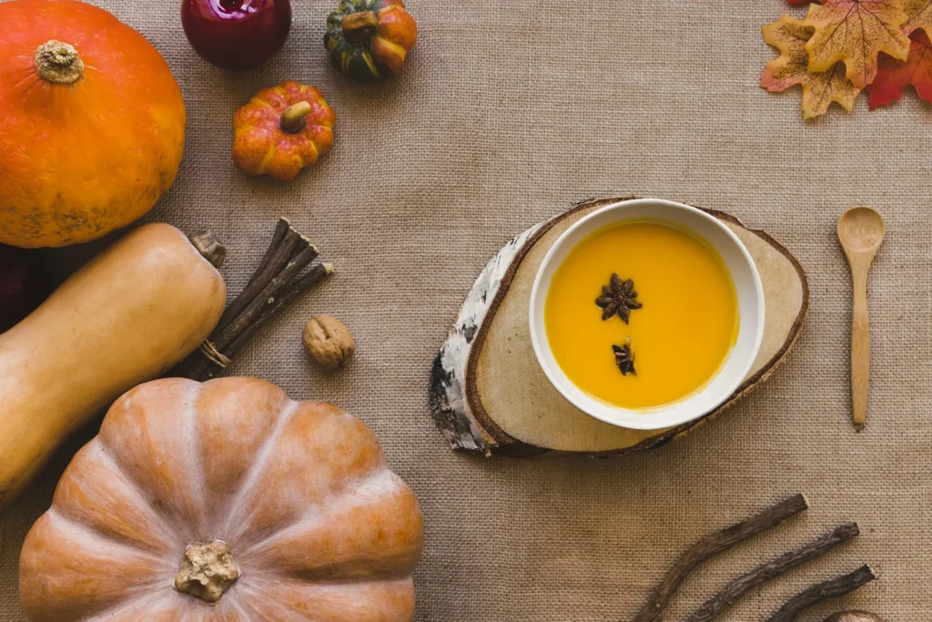 Herbstliches Stillleben mit Hokkaido- und Butternut-Kürbis, Schale Kürbissuppe mit Sternanis sowie Gewürz- und Holzdeko auf Jutestoff