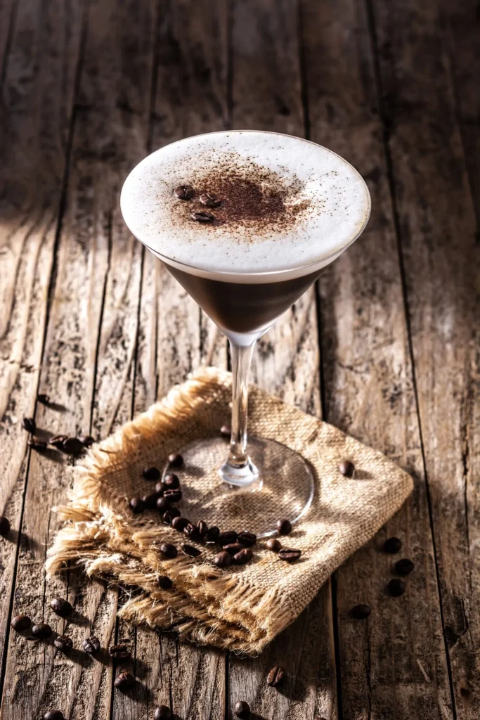 Espresso Martini mit feiner Schaumkrone und Kakaopulver, serviert im Martiniglas auf rustikalem Holztisch.