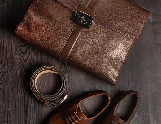 Edle Leder-Accessoires: braune Aktentasche, passender Leder-Gürtel und braune Herrenschuhe auf dunklem Holzhintergrund - hochwertige Geschenkideen aus Leder