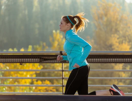 Frau joggt im Herbst auf einer Brücke vor bunt gefärbten Bäumen.
