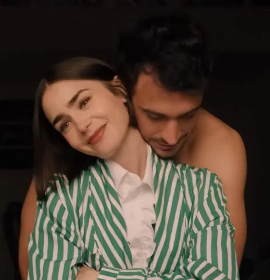 Emily in Paris Staffel 5 – Emily Cooper lehnt lächelnd im grünen Streifenblazer an Marcello Muratori, der sie von hinten umarmt. Emotionale Szene aus dem offiziellen Netflix-Trailer. Quelle: Netflix.