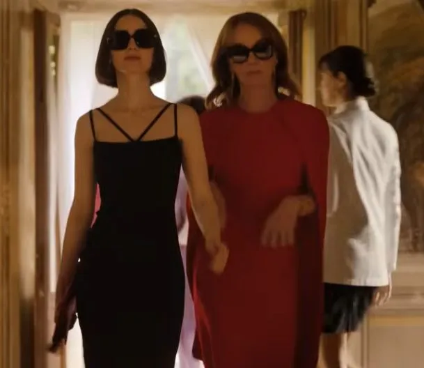 Emily in Paris Staffel 5 – Emily Cooper und Sylvie Grateau schreiten im Palazzo durch einen lichtdurchfluteten Flur, beide in eleganten Designer-Looks und Sonnenbrillen. Szene aus dem offiziellen Netflix-Trailer. Quelle: Netflix.