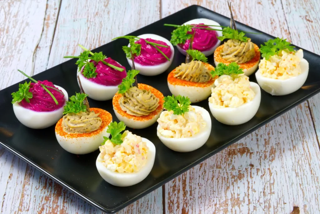 Gefüllte Eier und Deviled Eggs in verschiedenen Varianten mit Rote-Bete-Creme, Fischfüllung und klassischer Eiercreme, angerichtet auf schwarzer Platte