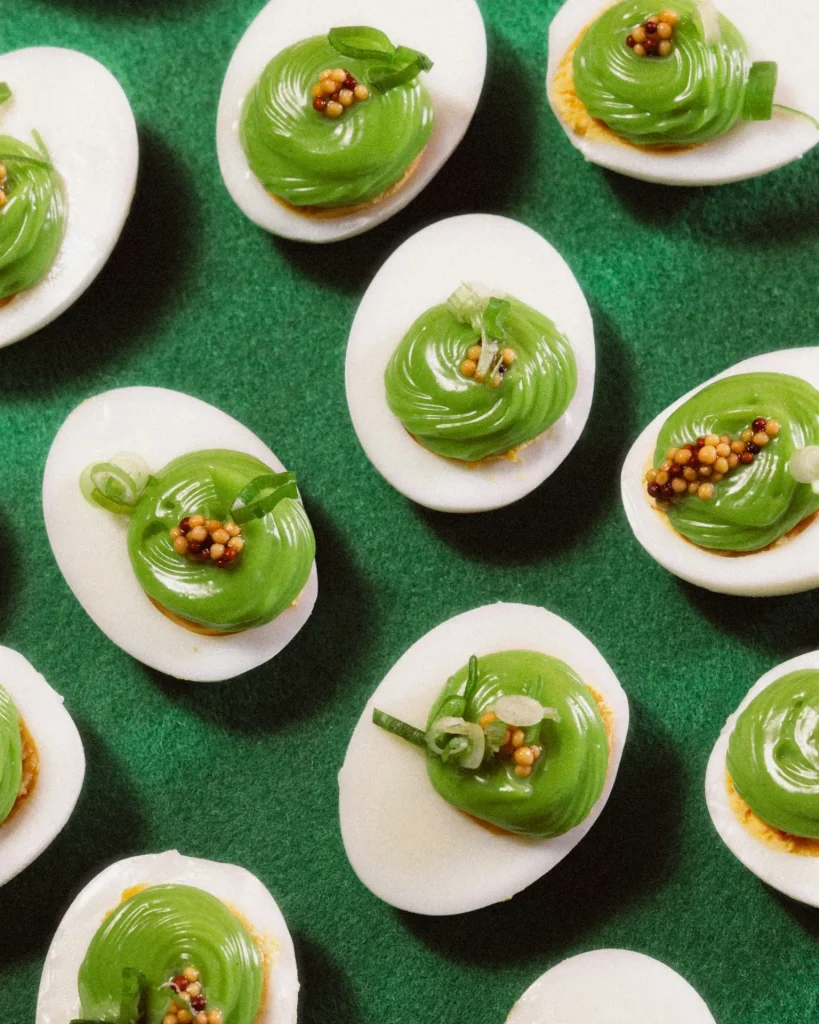 Deviled Eggs mit grün gefärbter Kräuter-Eigelbcreme, dekorativ gespritzt und mit Senfkörnern sowie Frühlingszwiebeln garniert