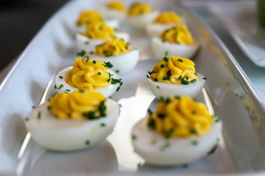 Deviled Eggs mit cremiger Eigelbfüllung, dekorativ mit Schnittlauch garniert, angerichtet auf einer eleganten weißen Servierplatte