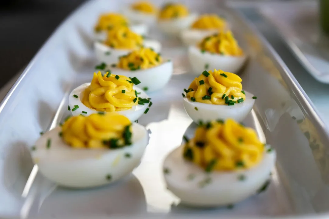 Deviled Eggs mit cremiger Eigelbfüllung, dekorativ mit Schnittlauch garniert, angerichtet auf einer eleganten weißen Servierplatte