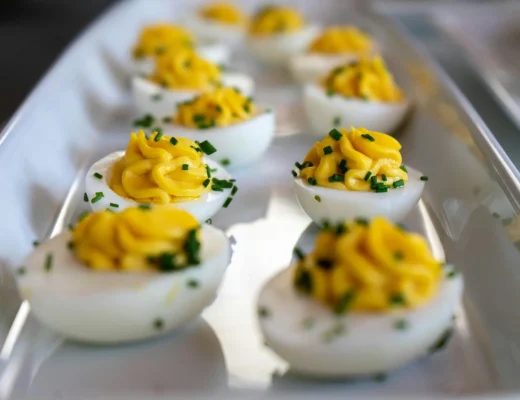 Deviled Eggs mit cremiger Eigelbfüllung, dekorativ mit Schnittlauch garniert, angerichtet auf einer eleganten weißen Servierplatte