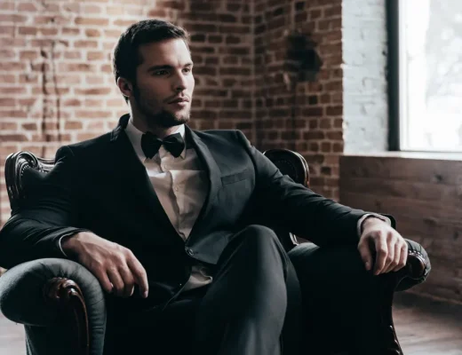 Ein Mann in einem schwarzen Anzug sitzt stilvoll in einem Sessel, repräsentiert Quiet Luxury