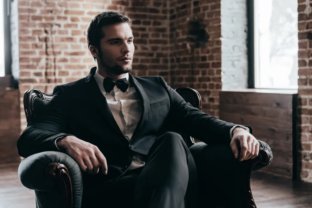 Ein Mann in einem schwarzen Anzug sitzt stilvoll in einem Sessel, repräsentiert Quiet Luxury