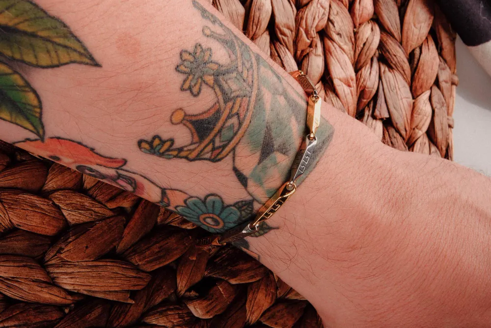 Farbige Tattoos am Unterarm kombiniert mit filigranem Armband als stilvolle Schmuckkombination
