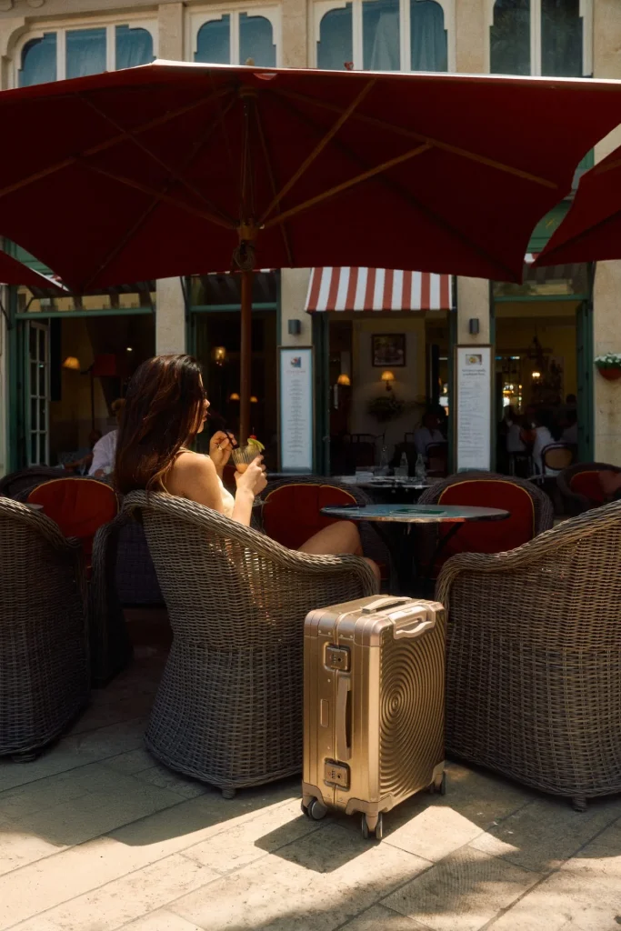 American Tourister Soundbox Alu Aluminium-Koffer vor Café-Terrasse