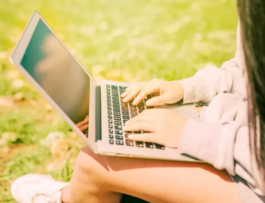 Person arbeitet mit Laptop draußen im Park bei sonnigem Wetter