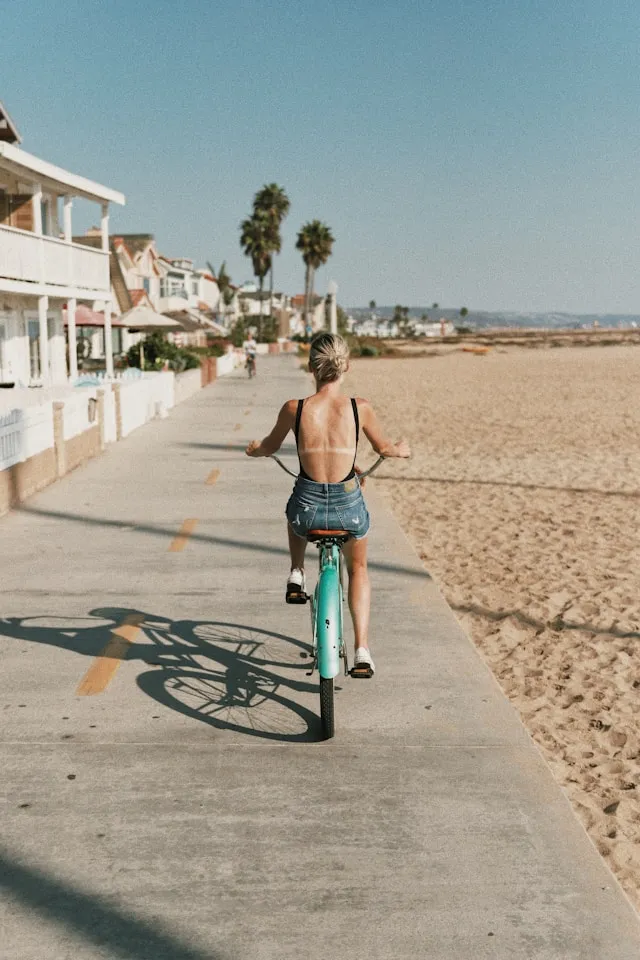 Frau fährt mit dem Fahrrad auf einer Strandpromenade – Symbol für regelmäßige Bewegung, Longevity und gesundes Altern.