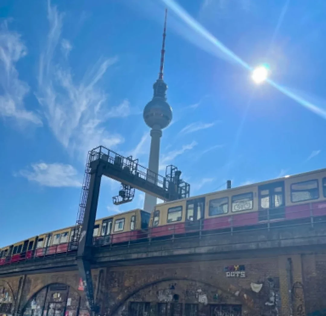 Rote U-Bahn, alte Stadtbahnbögen und der Fernsehturm im Hintergrund: Kaum ein Motiv zeigt Berlins Mischung aus rauem Alltag und großer Kulisse so direkt.