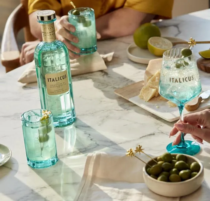 Italicus Rosolio di Bergamotto mit frisch gemixten Italicus Spritz, grünen Oliven und Parmigiano Reggiano auf einem gedeckten Tisch.