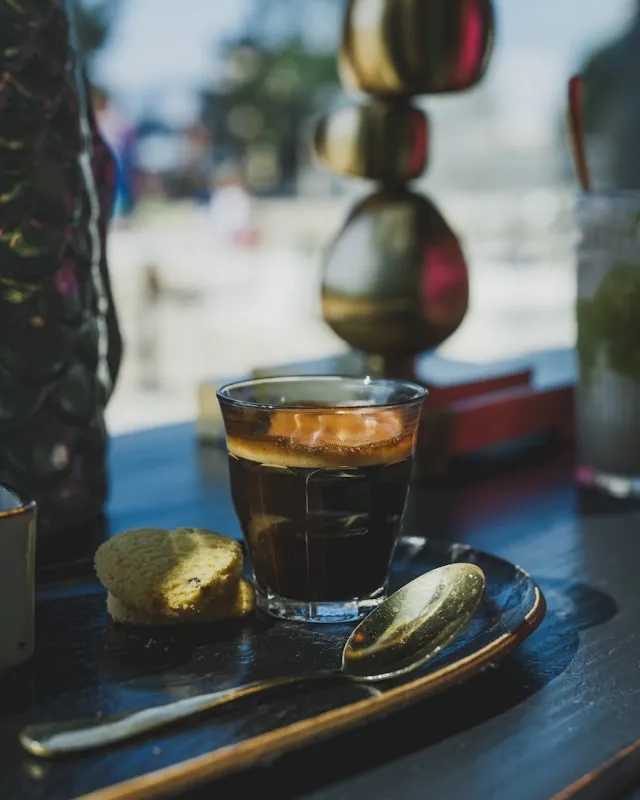 Espresso im Glas mit goldbrauner Crema, Löffel und Gebäck