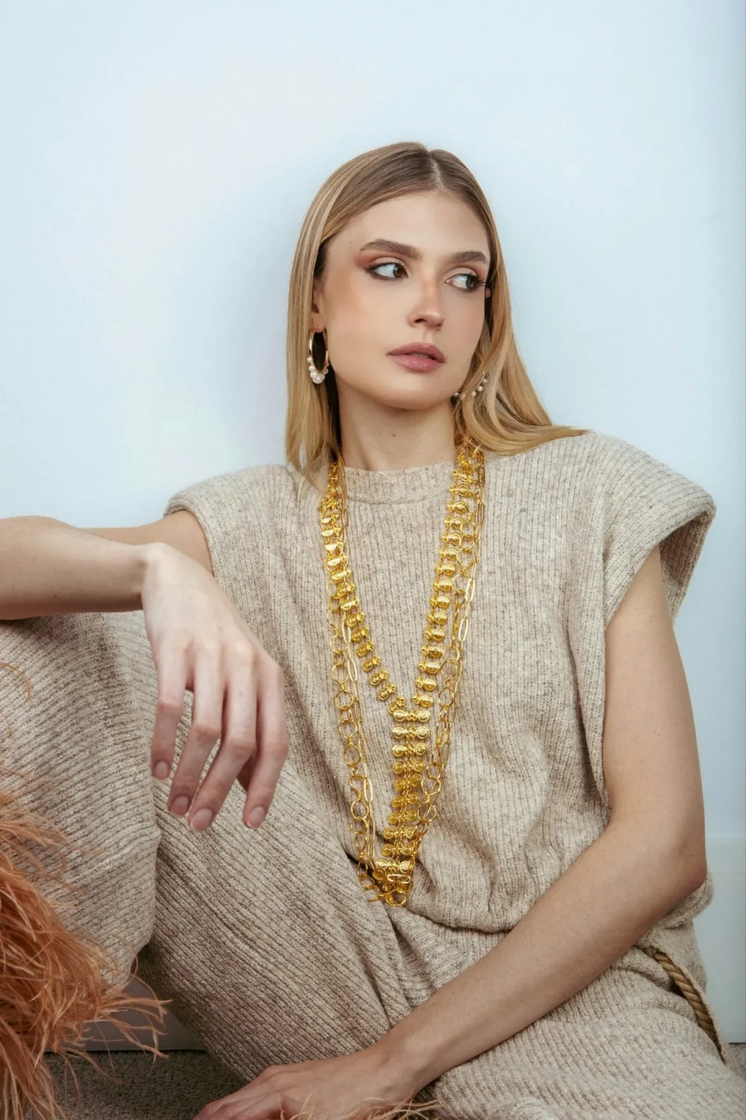 Model trägt mehrlagige Goldketten als XXL-Schmucktrend im Sommer 2026 zu einem beigefarbenen Stricklook.