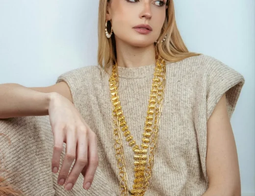 Model trägt mehrlagige Goldketten als XXL-Schmucktrend im Sommer 2026 zu einem beigefarbenen Stricklook.