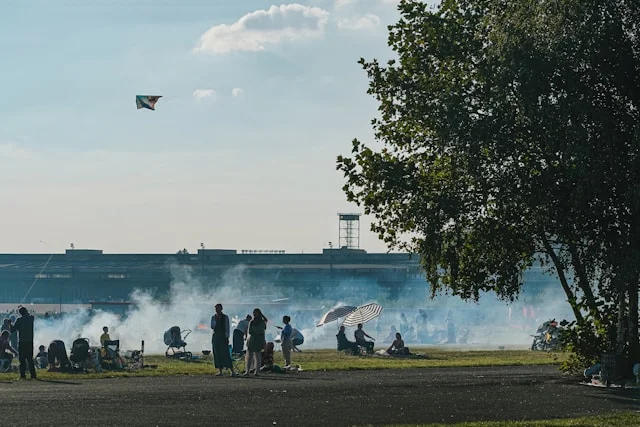 Menschen beim Picknick und Grillen auf dem Tempelhofer Feld in Berlin mit Drachen am Himmel
