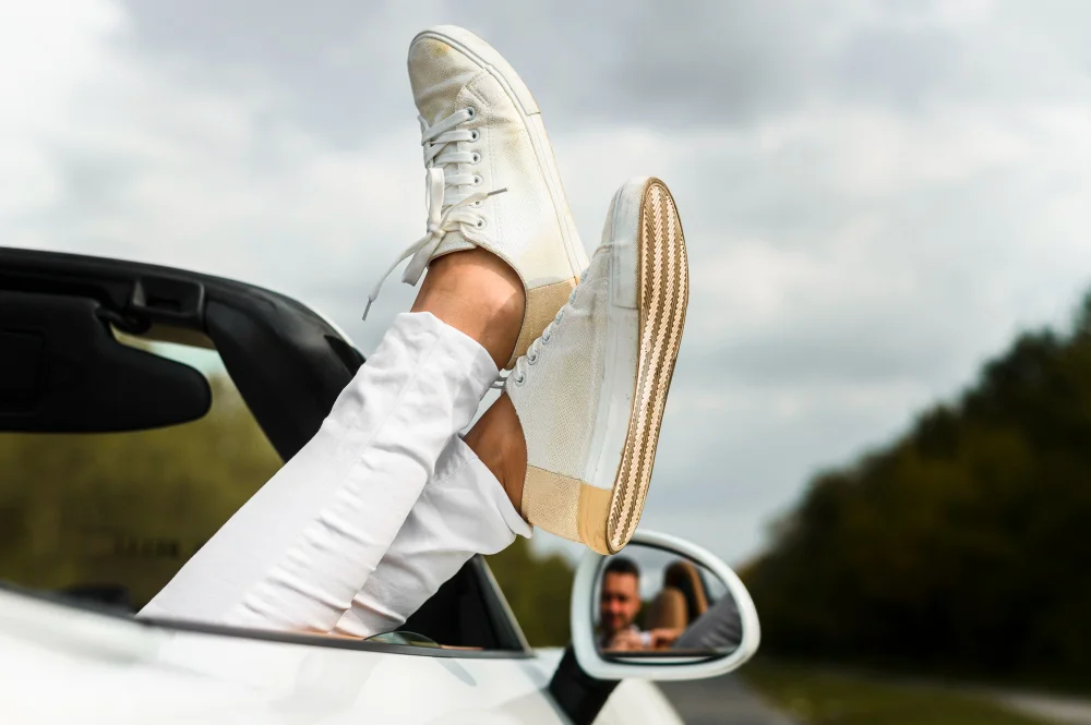 Weiße Sneaker an den Füßen einer Person in einem Cabrio