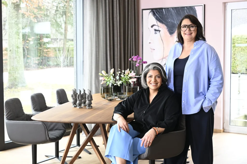 Sophia Lauton und Sahar Essmann im hellen Showroom mit Holztisch und grauen Sesseln