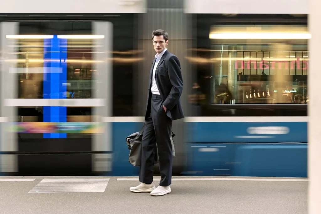 Mann im dunklen Anzug mit weißen Sneakern an einer Haltestelle