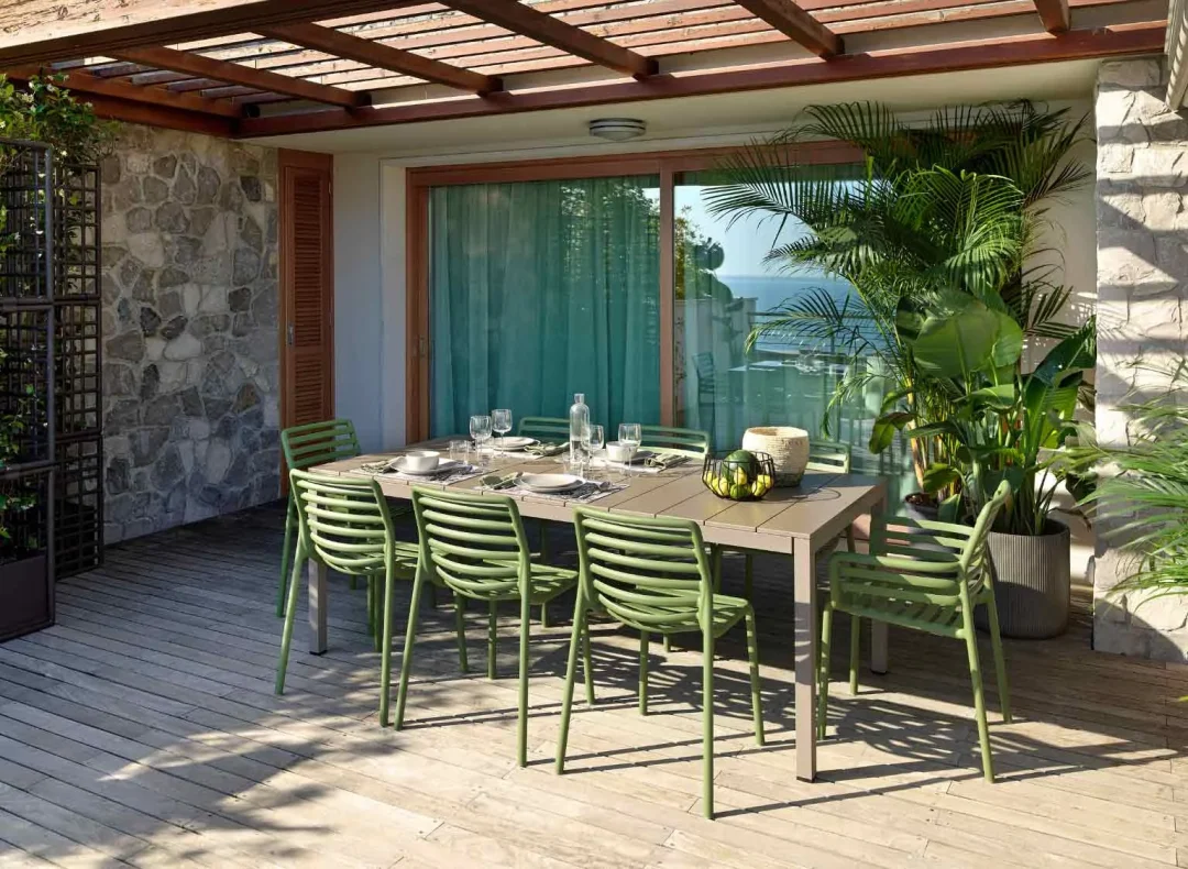 Gartentisch mit grünen Stühlen auf Holzterrasse unter Holzpergola mit Blick auf das Meer